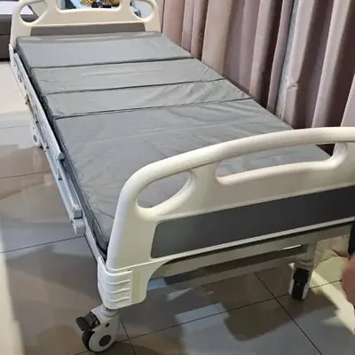 Hospital bed with a grey mattress beside bedroom curtains
